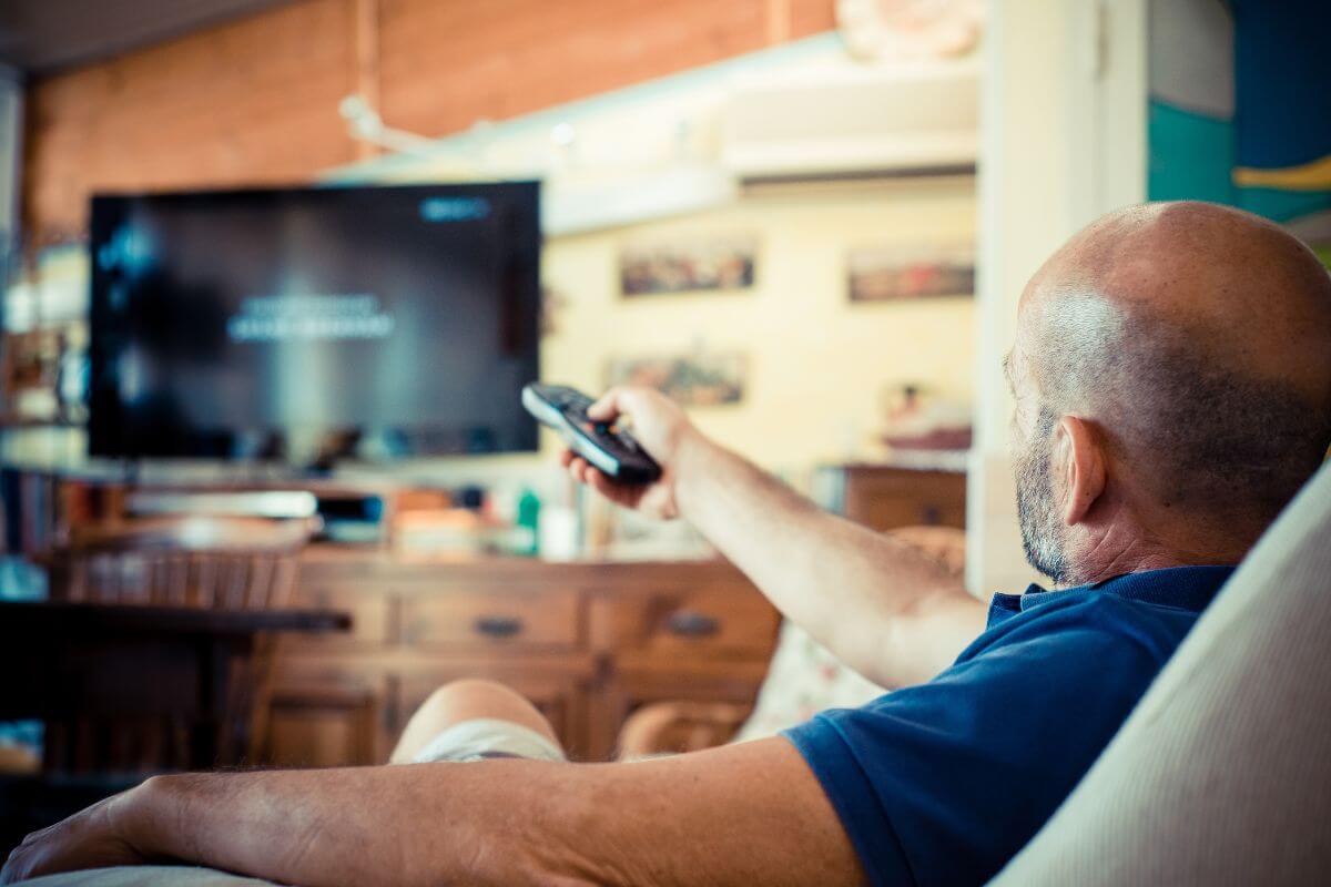 An image shows a man watching a TV.