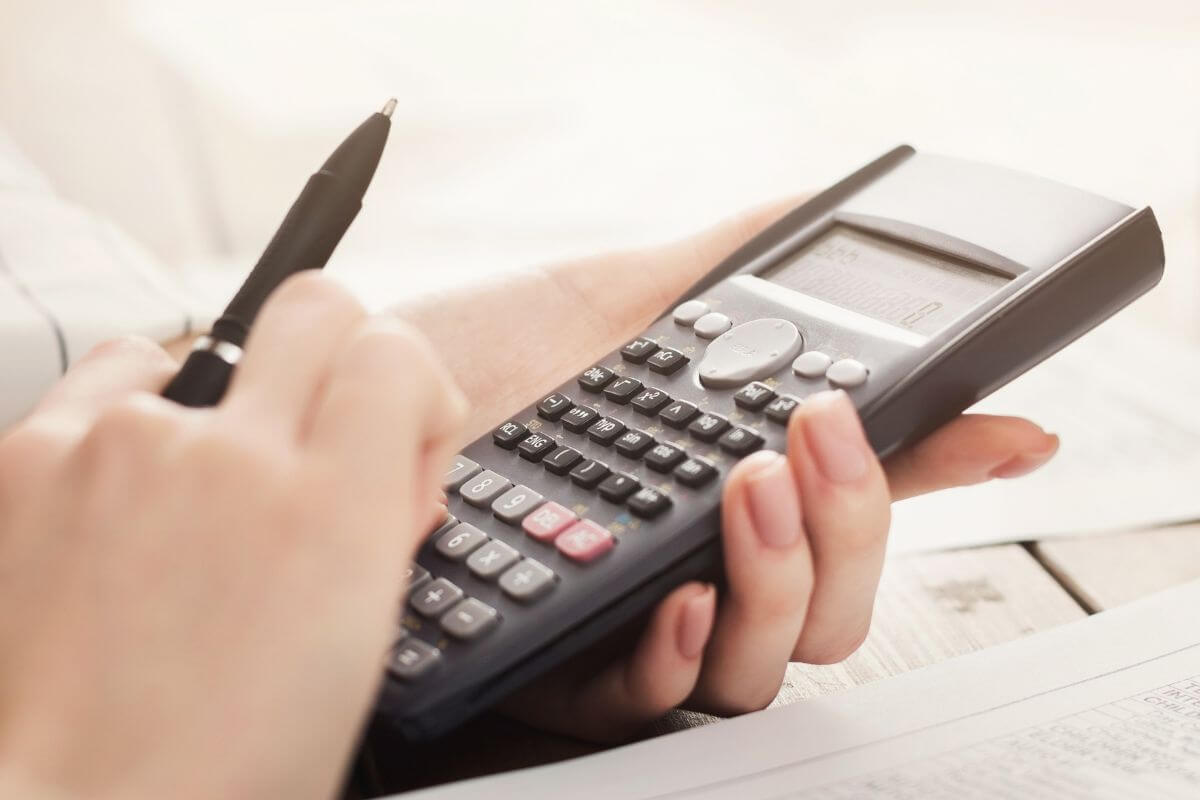Imagem da mão de uma mulher usando uma calculadora.