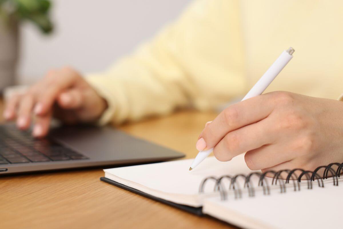 A picture shows a woman writing while using a laptop.