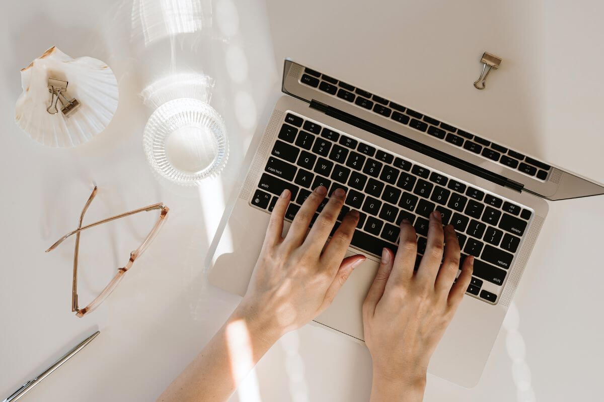 An image shows a woman's hand typing on a laptop.