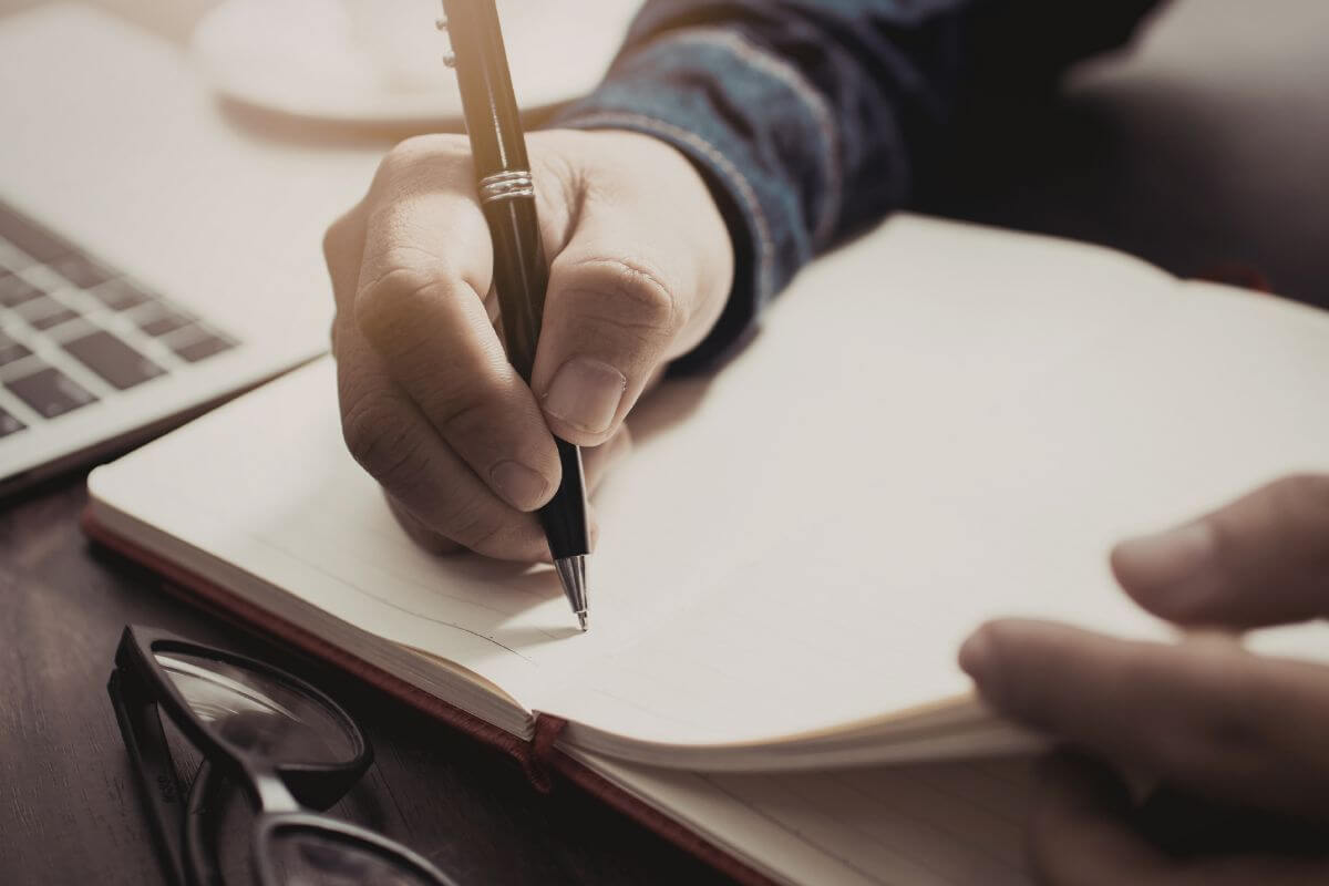 A picture of a man writing in the notebook.