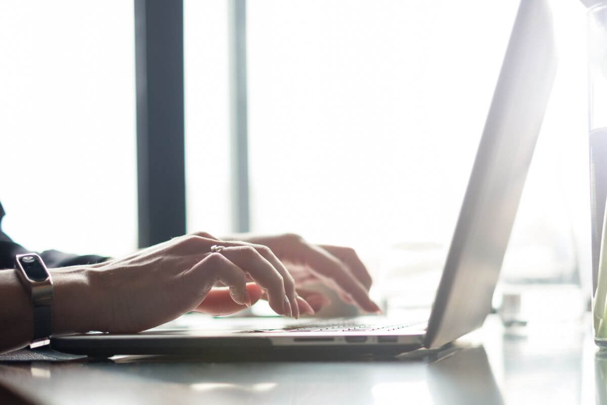 A photo shows a woman's hand typing on a laptop.