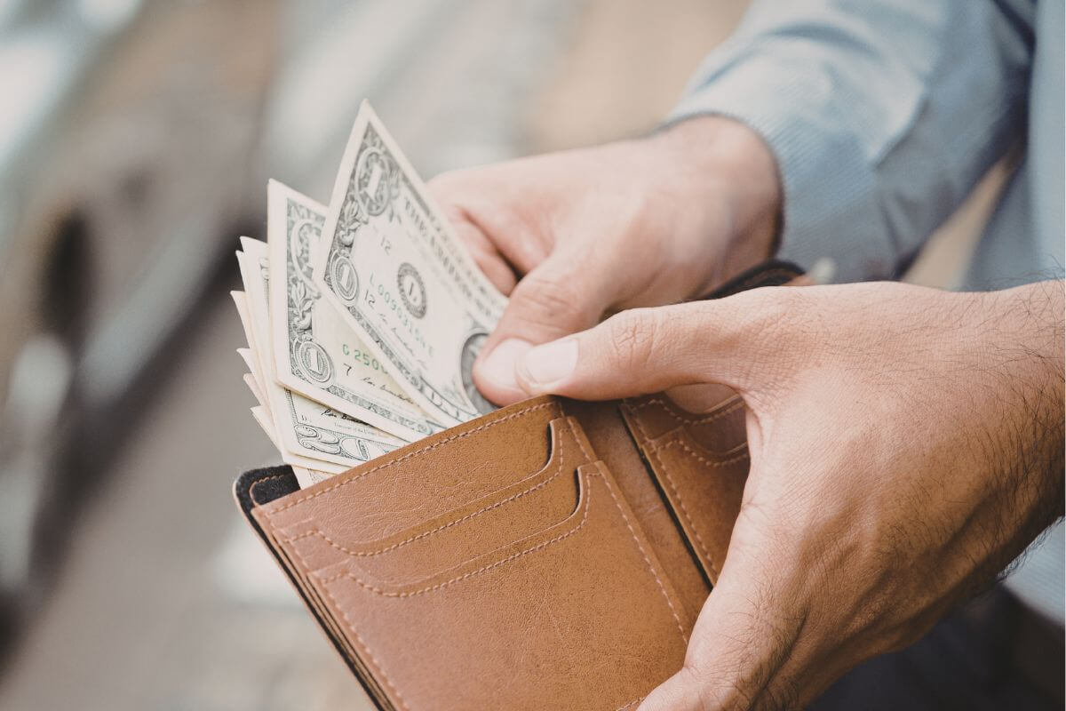An image of a man putting his money in his wallet.