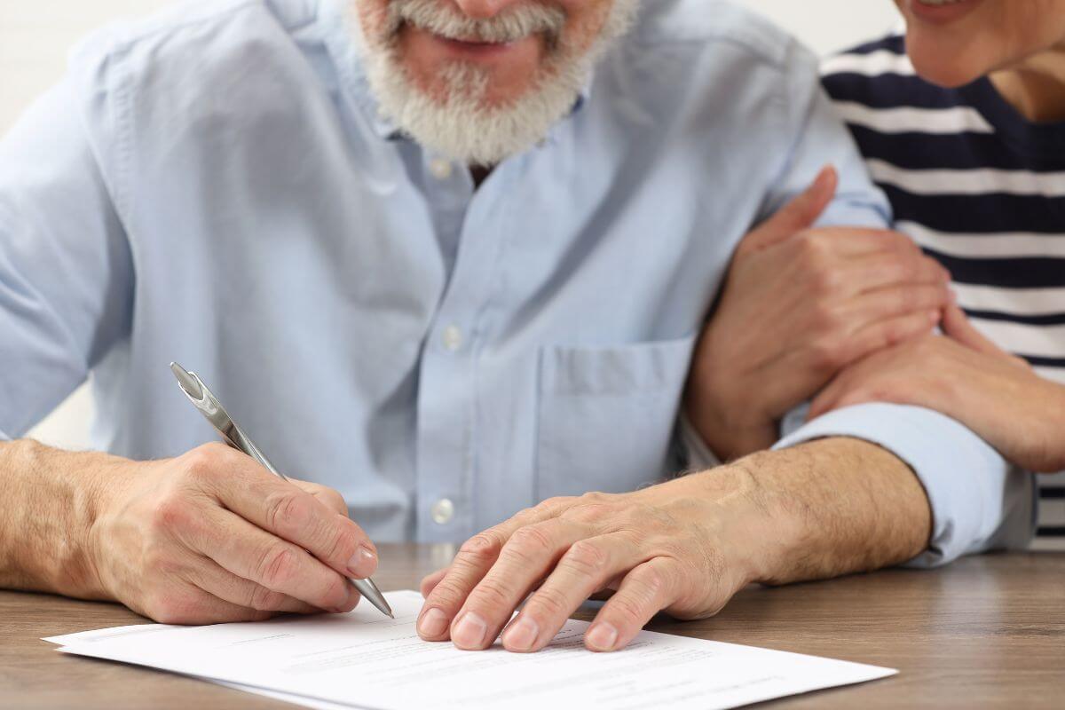 Uma foto mostra um casal de idosos assinando documentos.