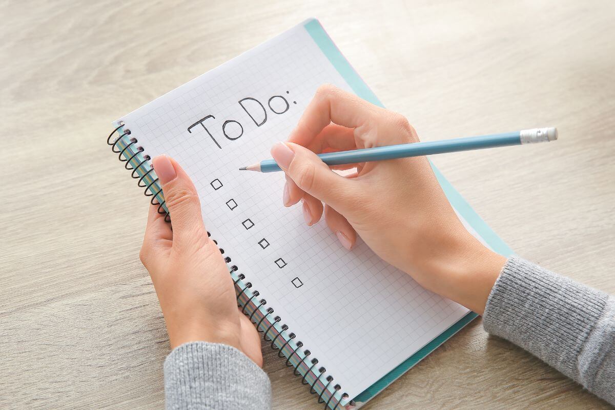 Uma imagem mostra a mão de uma mulher fazendo uma lista de tarefas.