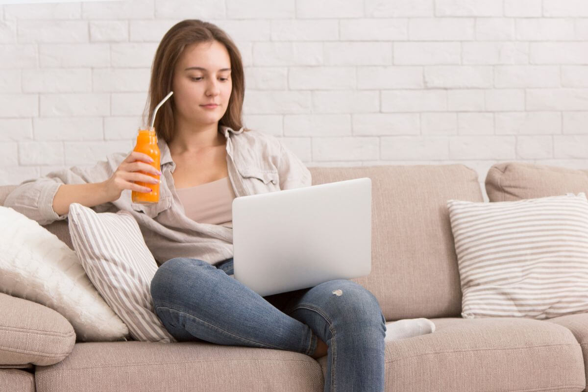 Imagem de uma mulher usando um laptop e bebendo suco.