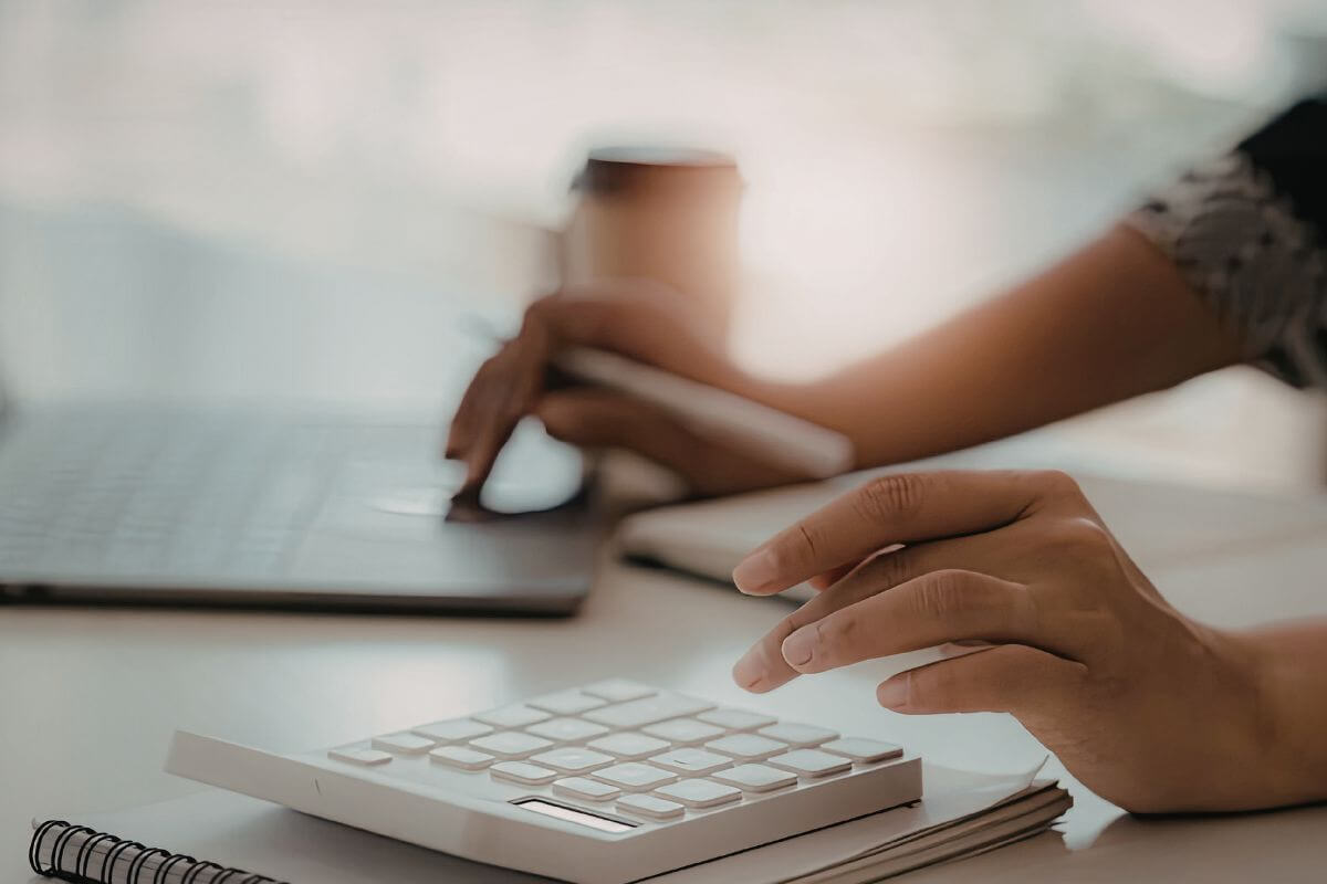 Uma imagem mostra uma pessoa usando um laptop e uma calculadora.