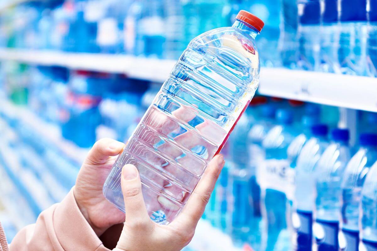 An image shows a woman picking up a bottle of water.