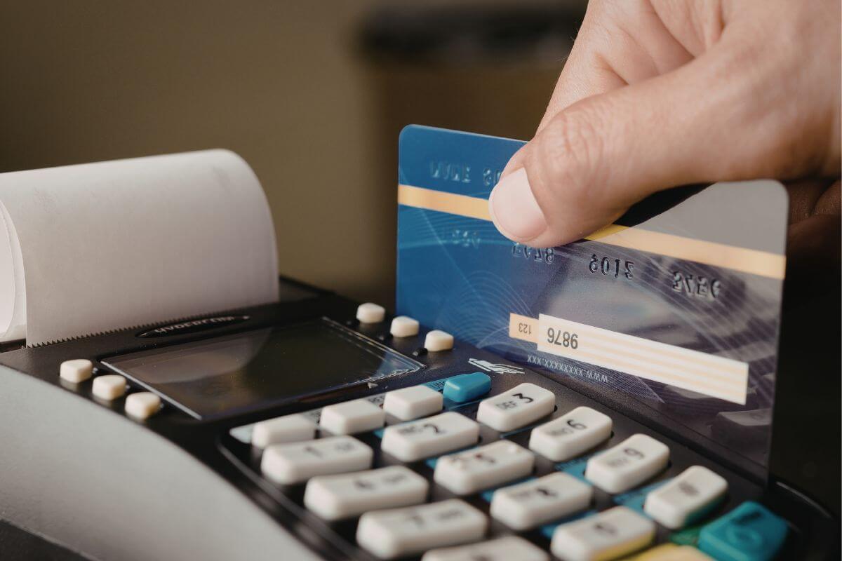 Uma foto mostra a mão de um homem passando um cartão de crédito.