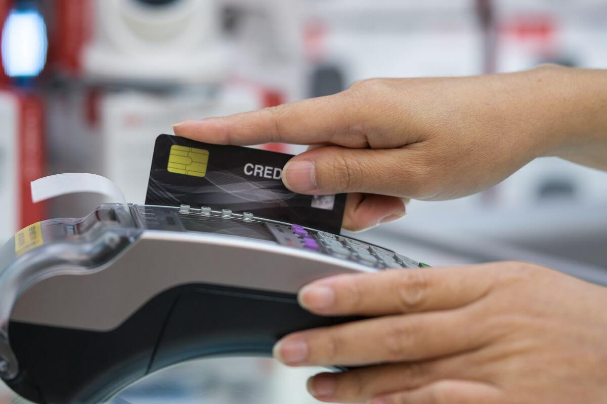 Uma foto mostra a mão de uma mulher passando um cartão de crédito.