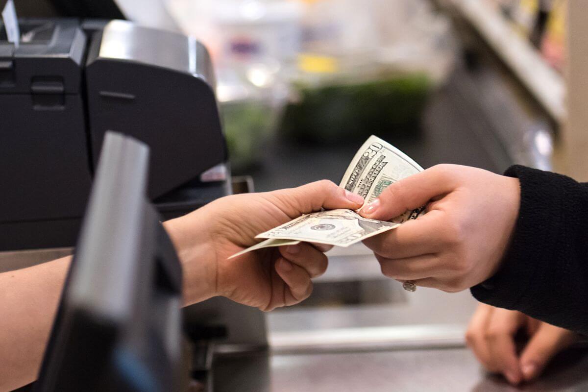 Uma imagem mostra a mão de um cliente pagando em dinheiro.