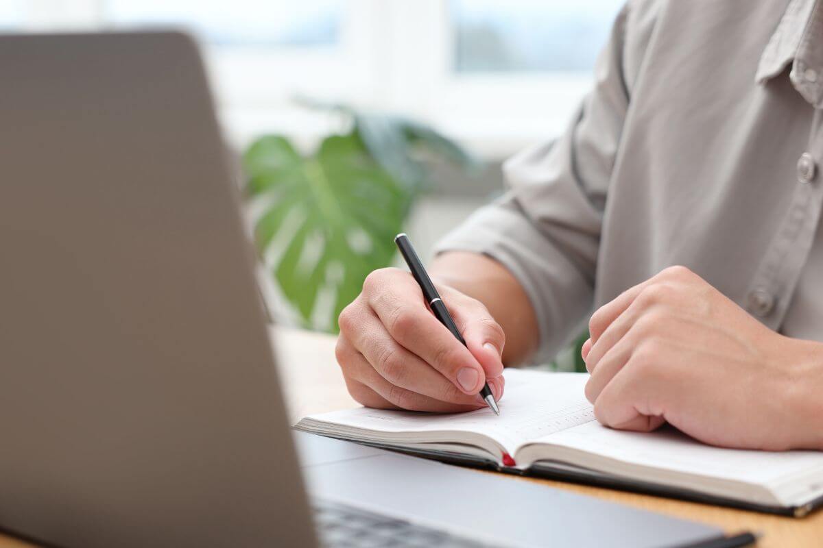 Uma imagem mostra um homem escrevendo em um caderno.