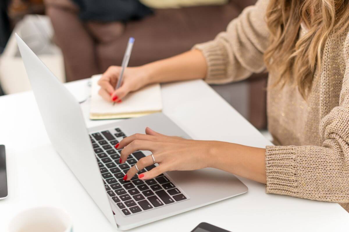 Uma foto mostra uma mulher usando um laptop e escrevendo.