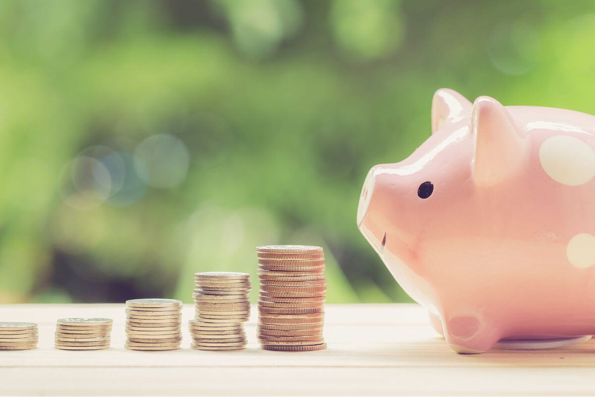 Uma imagem de um cofrinho e pilhas de moedas.