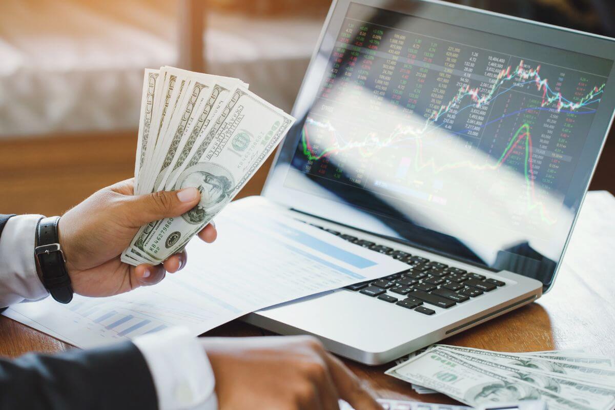 A picture shows a man holding money and a laptop with stocks.